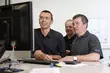 Three men working together in an office or technical environment, looking at a computer screen and discussing information.